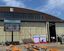 Zu sehen ist ein alter Flughafenhangar, vor dem eine große Leinwand steht, auf der ein Veranstaltungsprogramm angezeigt wird. Ebenfalls vor der Halle stehen Menschen und Bierbankgarnituren.